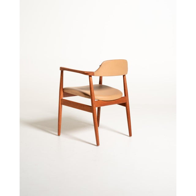 Teak frame with light proportions, contoured armrests, and beige faux leather upholstery on the seat and back....