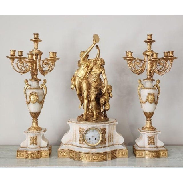 A palatial 3-piece French garniture set of documented "jewelry-grade" quality. Centered by a 32" clock featuring a figural...