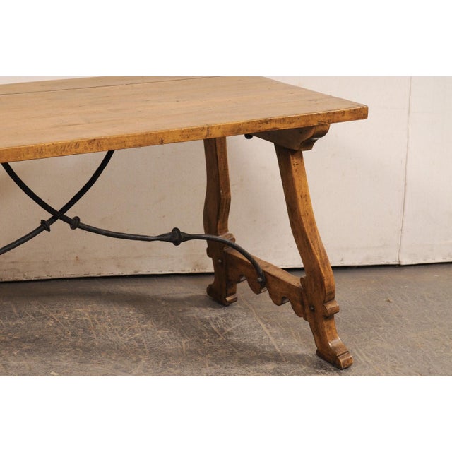 An Italian-style wooden trestle-leg table, with forged-iron stretcher, by high-end American furniture maker Michael...