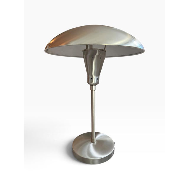 Striking vintage table lamp with a sleek silver-tone metal dome shade and streamlined pedestal base. The dramatic...
