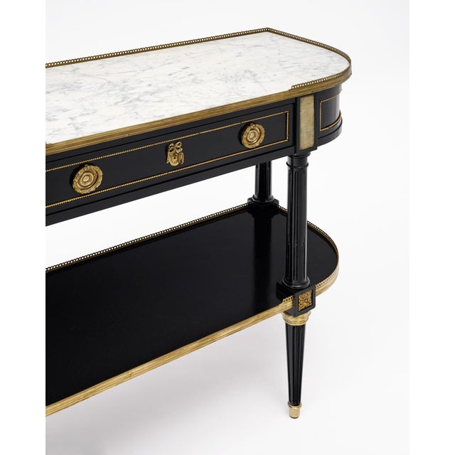 An elegant French Louis XVI style console table constructed in ebonized wood with a white marble top and extensive gilt-...