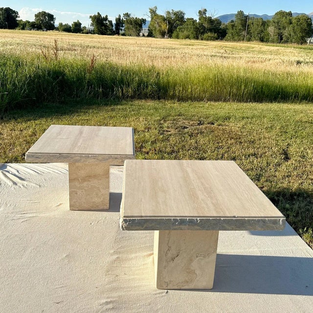 Gorgeous set of two square travertine side tables, each resting on a single center pedestal. Each tabletop features rough...