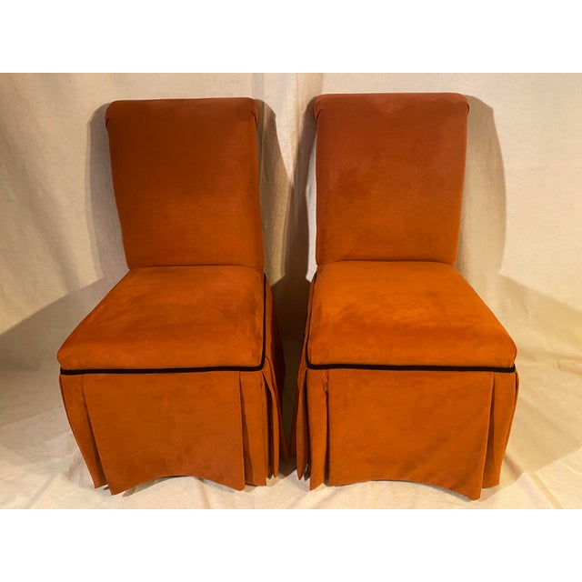 A finely crafted pair of rolled back slipper chairs with fully lined box pleat skirting, upholstered in high quality burnt...