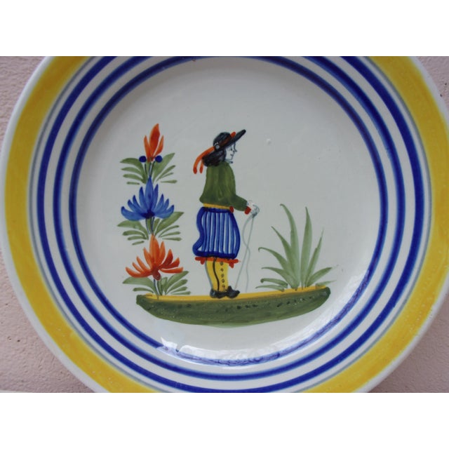 A French faience plate with a farmer in the costume with flowers signed Henriot Quimper, circa 1930. Colorful yellow...