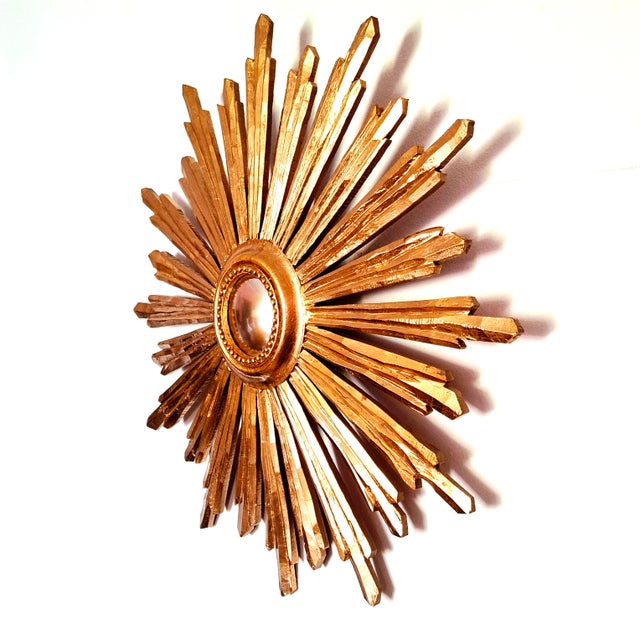 A finely crafted sunburst mirror made of gilded wood, distinguished by its rhythmic arrangement of elongated rays and...