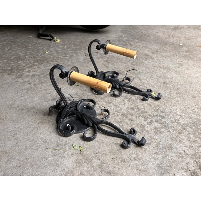 Matching set of single-arm black wrought iron sconces with scrollwork backplates and beeswax-style candle covers; Spanish...
