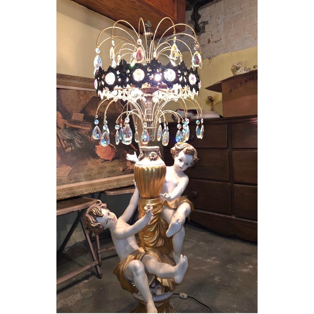 The image shows a vintage Italian classical-style table lamp featuring porcelain cherub figures and an ornate crystal-drop...
