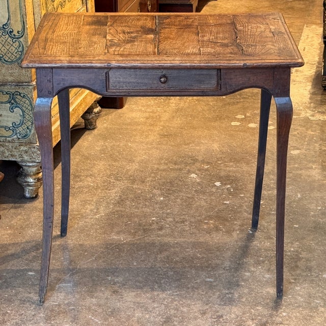 A 19th century French oak side table with a single drawer, a shaped apron, and slender cabriole legs. The plank top has a...