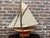 A vintage pond yacht, sloop design with a main mainsail and multiple smaller head sails. The hull is wooden with a cream...