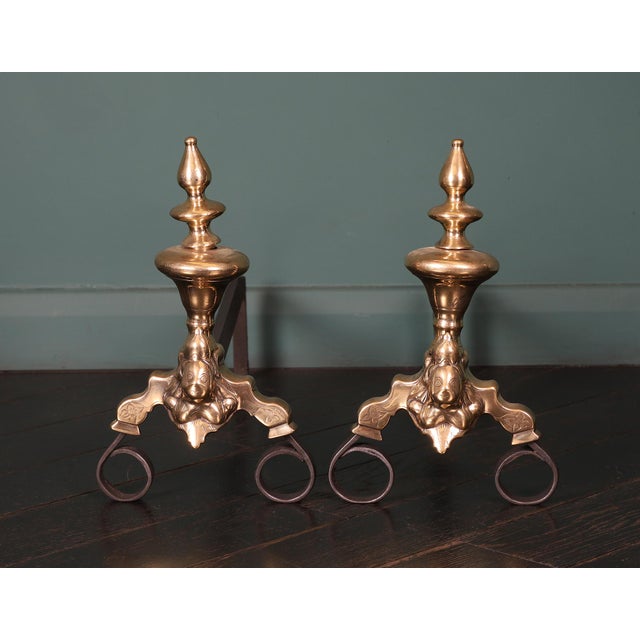 A pair of 18th century Dutch brass and wrought andirons. The vase shaped finials are supported on scroll feet faced with...