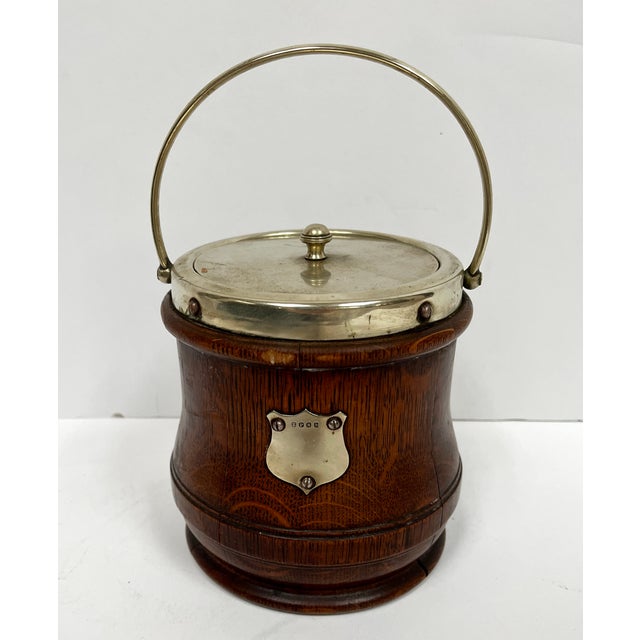 Imported from England. Classic oak biscuit barrel with porcelain liner. Silver rim, handle, cover, and crest labeled...