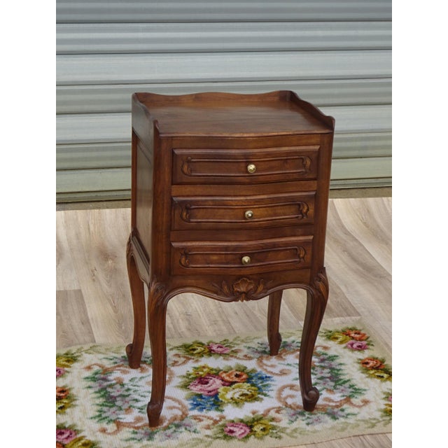 Elegant bedside table with three drawers and raised edges on three sides of the top. Tall, slender legs with cabriole...
