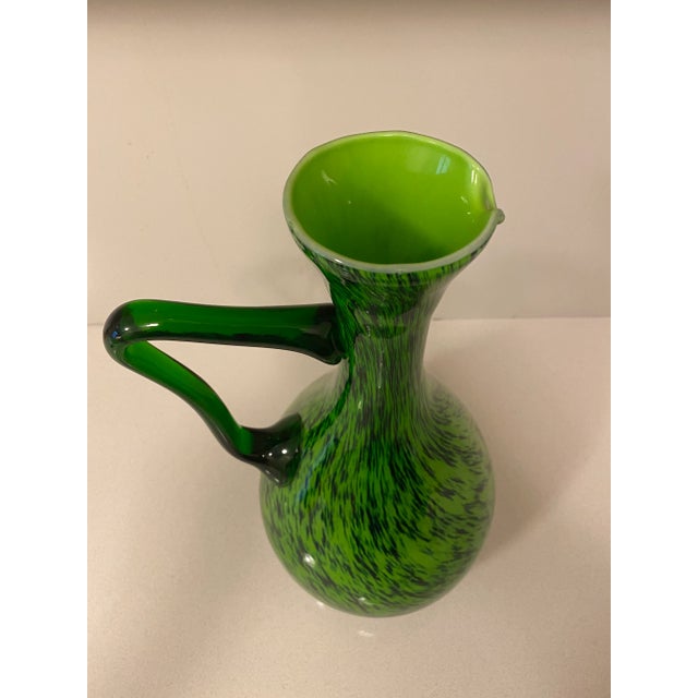 Very unusual pattern of a classic mid century cased glass pitcher. The handle is clear green glass with the body of the...