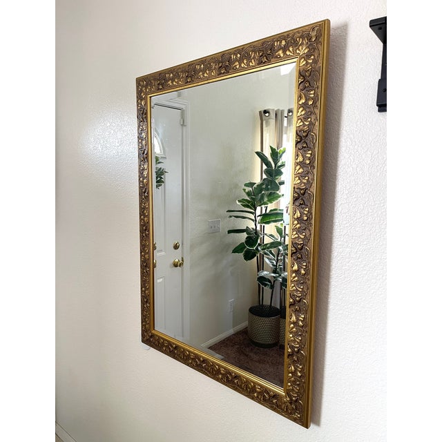 Beautiful European detailed vintage mirror featuring a carved wooden frame with floral and vine motif, a gilt gold finish...