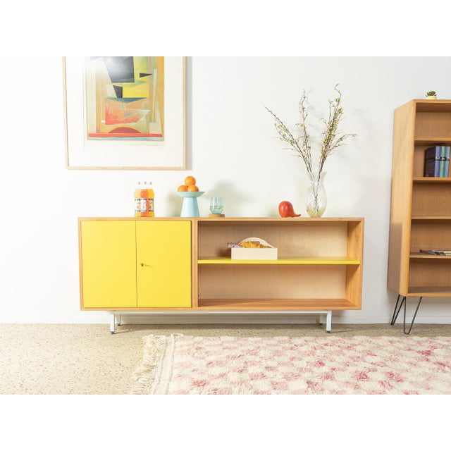 A wonderful sideboard from the 1950s. The body is made of bleached walnut veneer with two cabinet doors, two shelves, and...