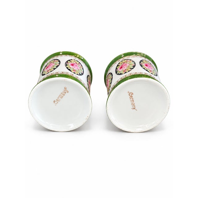 Description: A matching pair of small German mugs decorated with pink rose bouquets in black oval medallions. Deep green...