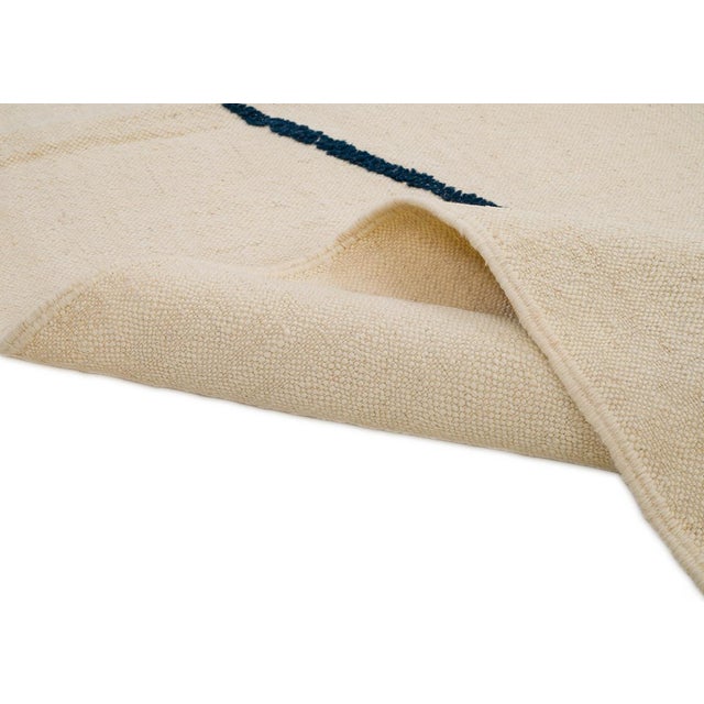 A single graphic silhouette hangs from two converging charcoal lines on an open ivory field, distilling this handwoven rug...
