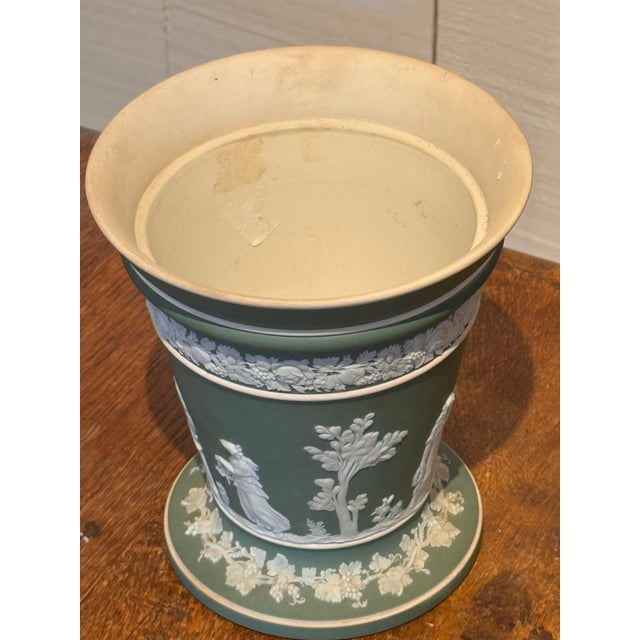 A Wedgwood green jasperware jardinière with white relief decoration of neoclassical figures, floral swags, and vine...