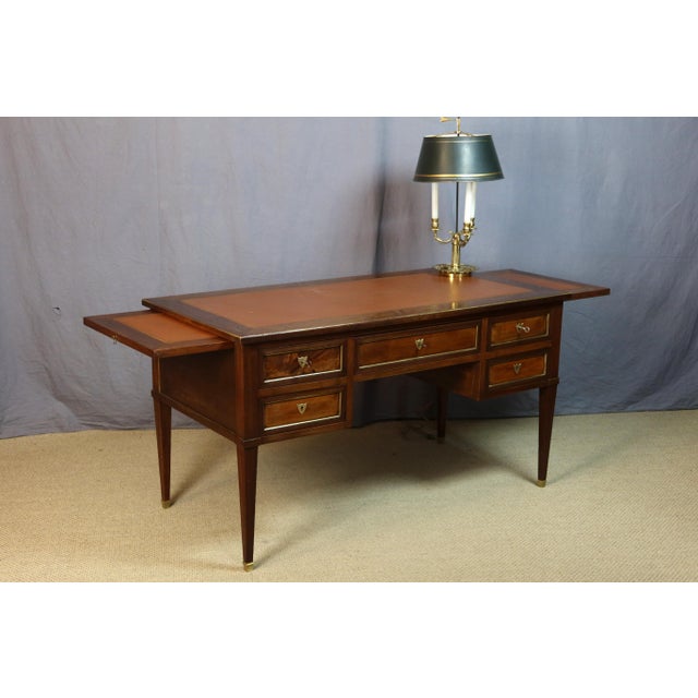 A Louis XVI style walnut desk adorned with brass moldings and featuring five drawers. The legs terminate in gilt bronze...
