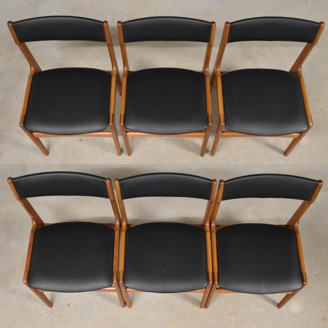 A set of six mid century modern solid teak dining chairs with black vinyl back rests and seats. Seat height is 17.5”. Made...