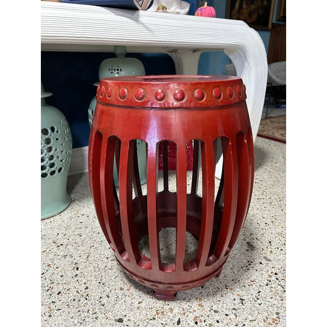 This wooden drum stool features an openwork barrel-shaped frame, decorative raised details, and a rich red painted finish....