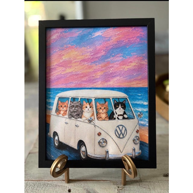 Charming framed art print featuring a white vintage van with five playful cats against a pastel pink and blue seaside sky....