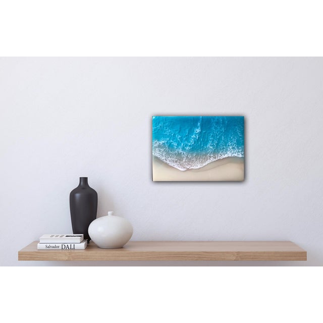 This artwork presents a serene aerial view of a white sand beach, where vibrant turquoise waves gently meet the shore. The...