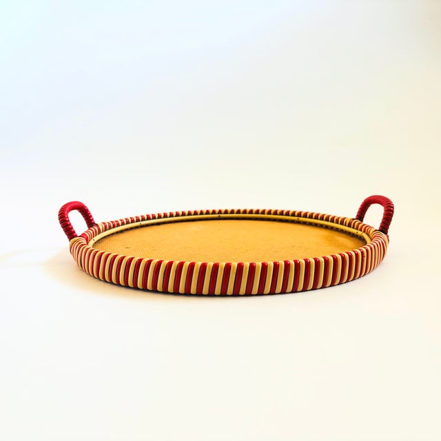 A large circular mid century tray. Features a woven rim and handles made of beige and red plastic. The center is made of...