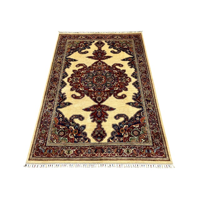 An ornate central medallion anchors this natural-dyed wool rug against a warm beige field. Deep red floral borders and...