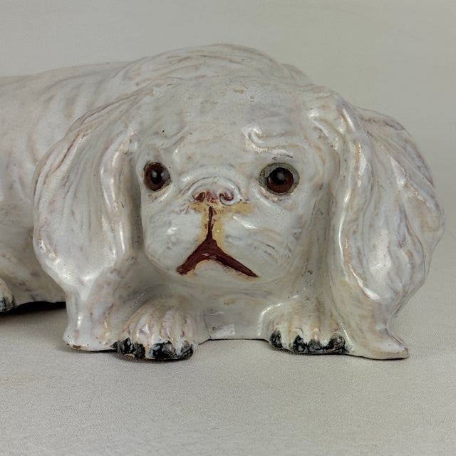 A rare to market vintage French white tin glazed terracotta sculpture of a pekinese dog with glass eyes. It is stamped...