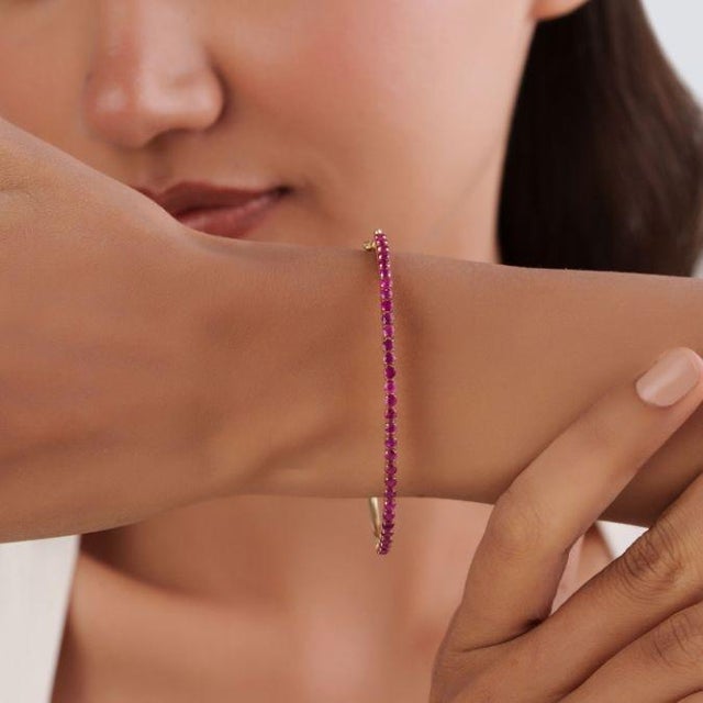 This elegant bangle bracelet features 2.43 carats of natural rubies, set in 14k yellow gold. Each measuring approximately...