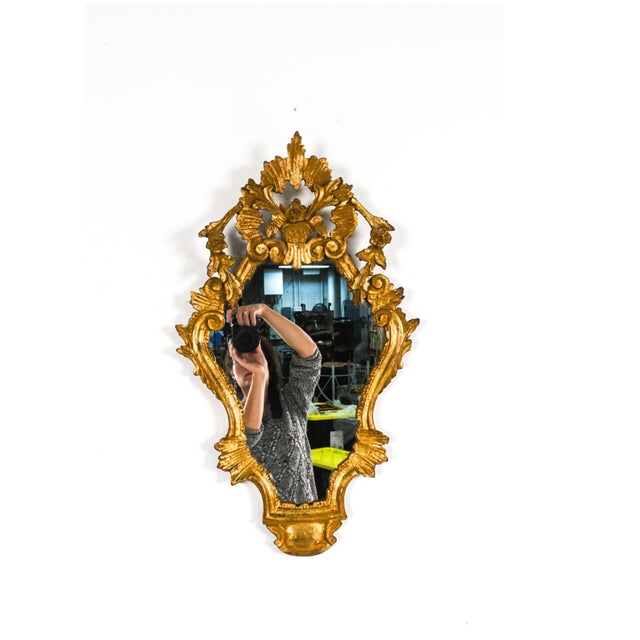 A matching pair of Rococò style giltwood wall mirrors with a warm, aged patina, shield-shaped plates set, elaborately...