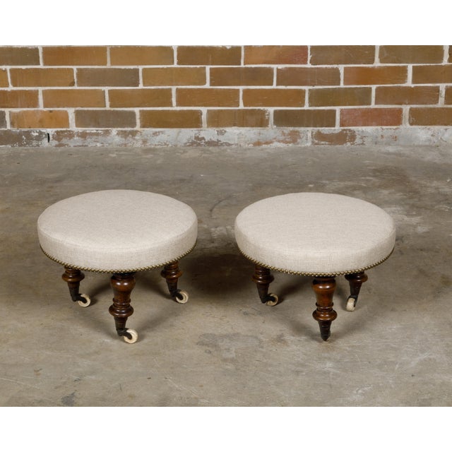 A pair of English mahogany stools from the 19th century with turned legs resting on casters and upholstered seats. This...
