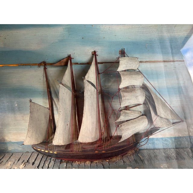 A large, handcrafted maritime diorama depicting a sailing ship under full sail, presented in a deep, painted wooden...
