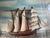A large, handcrafted maritime diorama depicting a sailing ship under full sail, presented in a deep, painted wooden...