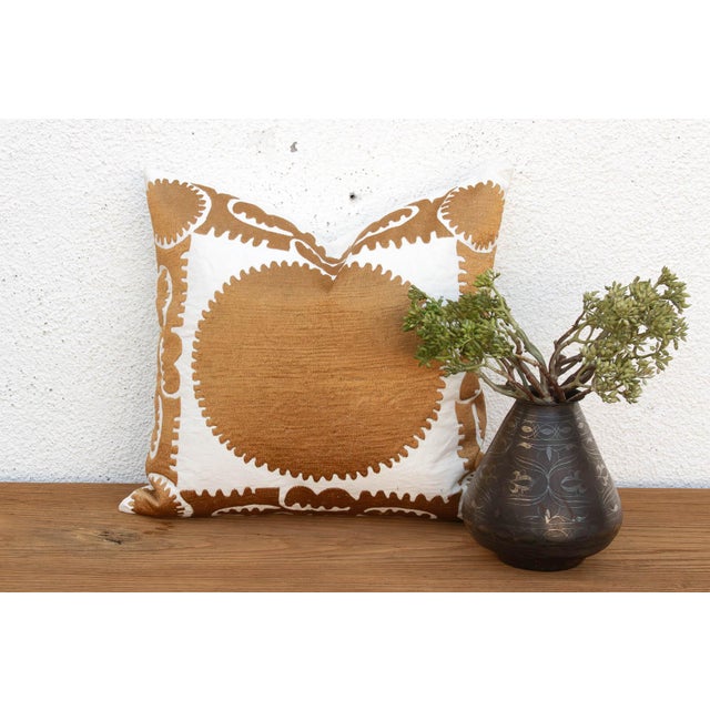 A large sun-disc medallion, hand-embroidered in a rich gold-tan thread, radiates from the center of this pillow — its...