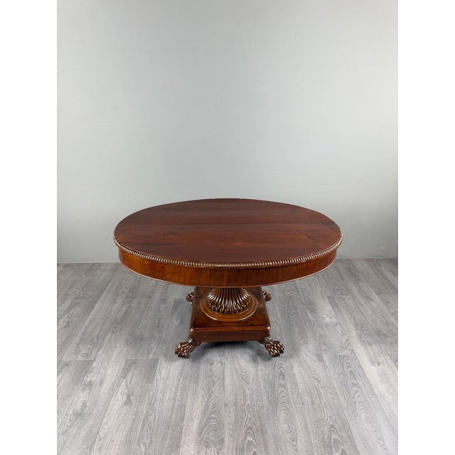 An elegant oval empire-style table dating from the 19th century. it features a beautiful oval top with a beaded border,...