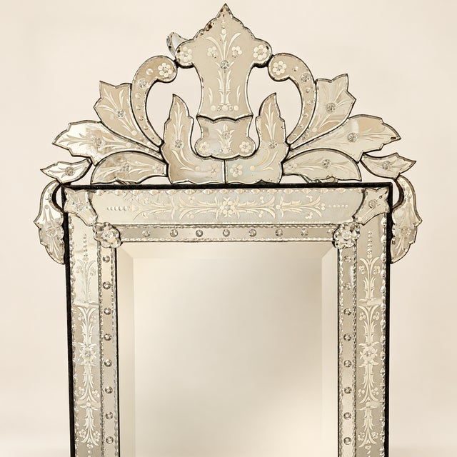 A Venetian style wall mirror made almost entirely of glass. The beveled center plate is framed by etched mirror panels of...