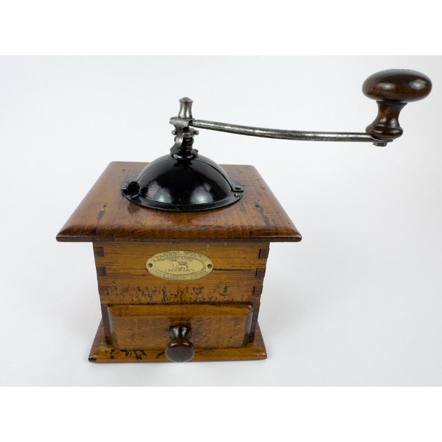 Vintage manual coffee grinder produced by Peugeot Frères, featuring a solid wooden body, metal hopper, and original hand-...