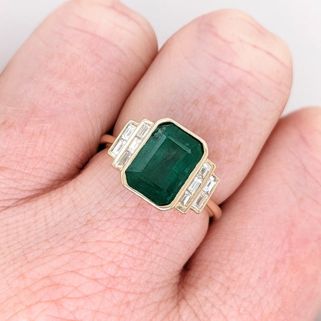 An emerald sits in a rich green at the heart of this solid 14K yellow gold ring, flanked by ten earth-mined diamonds....