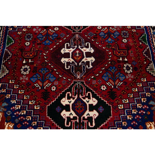 Beautiful Vintage Shiraz hand-knotted Wool rug with a red color field. This piece has a beige frame and multicolor accents...