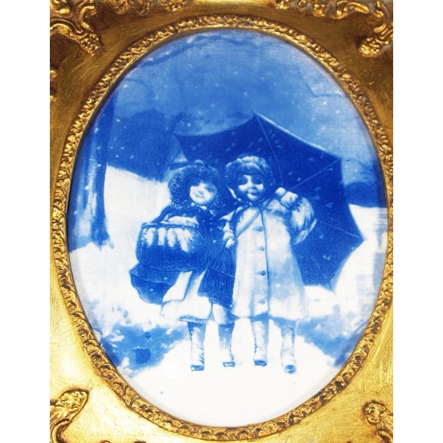 An antique blue and white Delft plaque of children in rain with umbrella. Contemporary gold frame. Plaque is...
