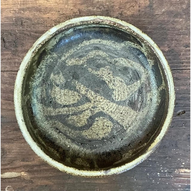 This shallow pottery bowl presents a rounded, gently sloping profile, its walls curving smoothly from a wide, unadorned...