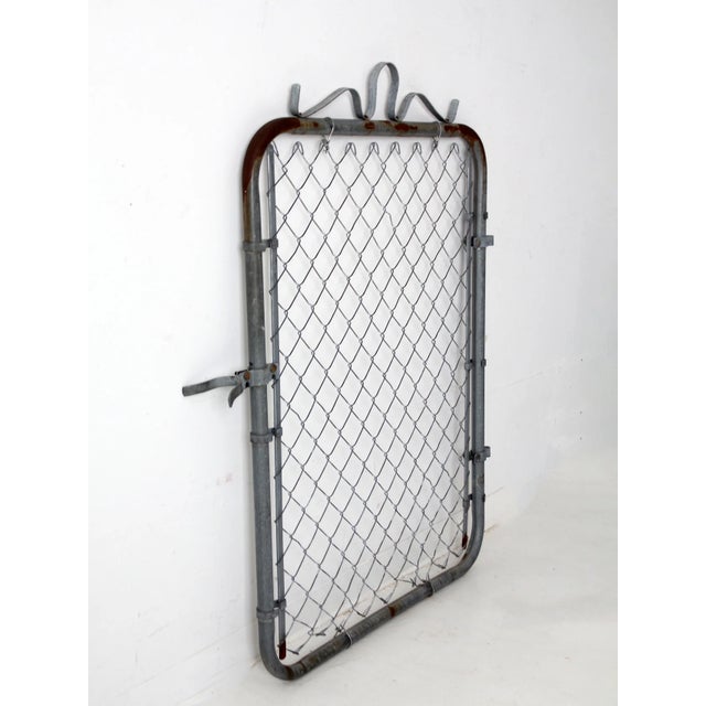 A galvanized steel chain link gate from the mid-20th century with rounded corners and an arched top formed by looping...