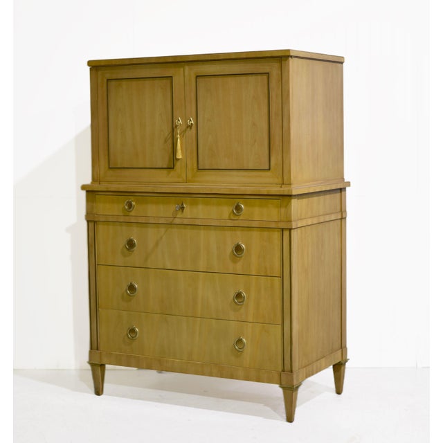 Mid century Directoire style highboy dresser by John Widdicomb with a blonde wood finish and a tall, stepped case. Two...