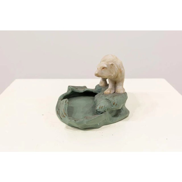Art Deco style and period ashtray, made of soft ceramic paste. It represents a polar bear on a bluish-green cave that...
