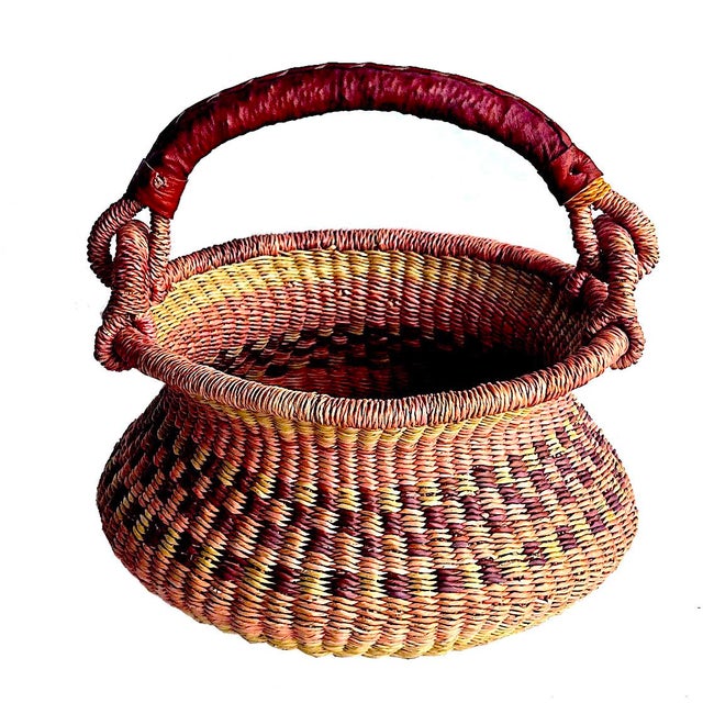 Offered is a handwoven Bolga basket crafted in Ghana from durable elephant grass that features a leather-wrapped handle....