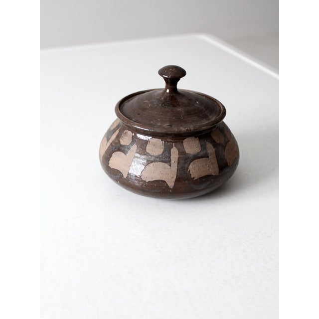 This vintage studio pottery jar features a rich, dark brown glaze with unglazed abstract motifs around the body. The...