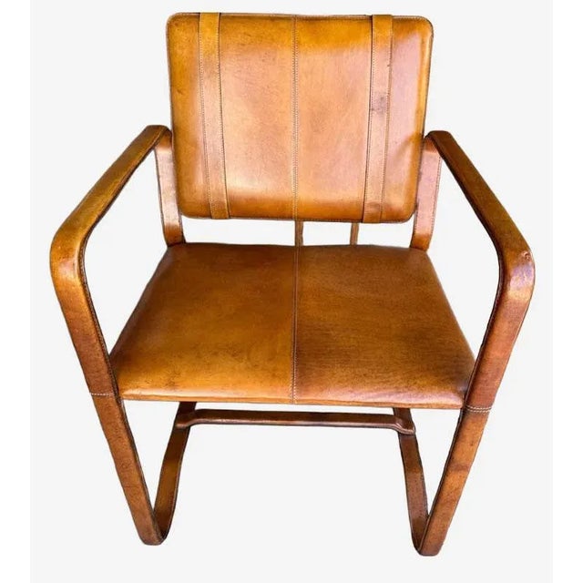 Beautifully patinated camel color leather chair with two matching antiqued cast-brass buckle details on the back. The...