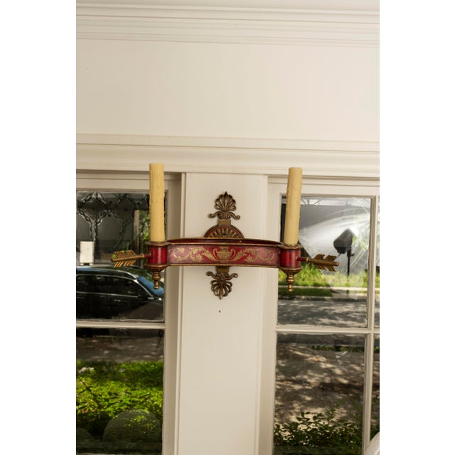 Large pair of French Empire style or Neoclassical style red and gold decorated bronze and tole two-light sconces. This...